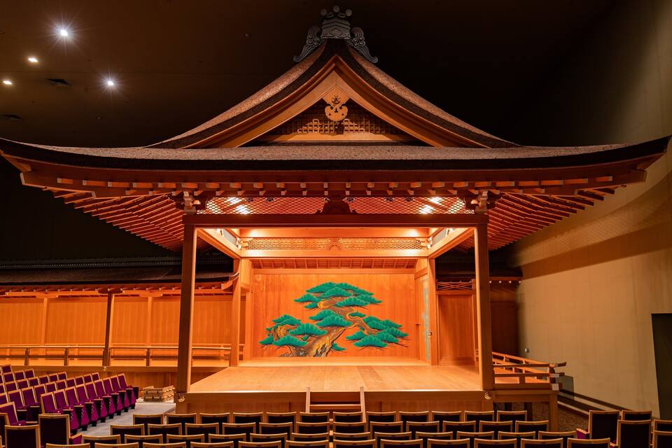 A traditional wooden stage with a painted tree mural, surrounded by rows of purple chairs.