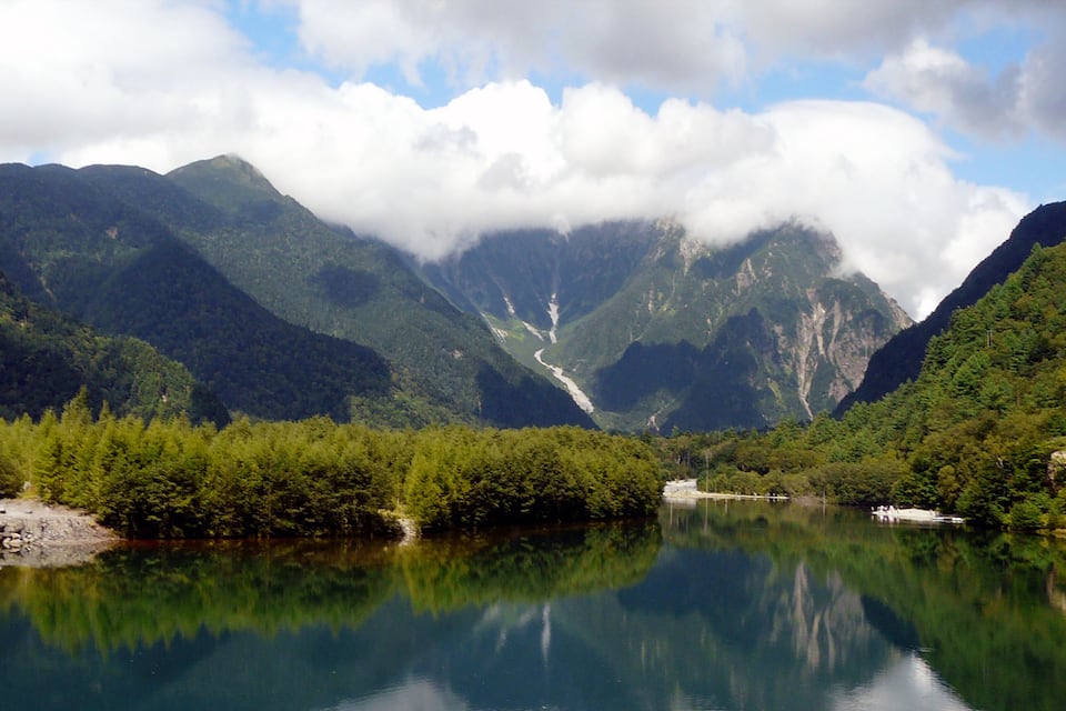 A mountain lake with reflections, surrounded by dense forest and steep cliffs.