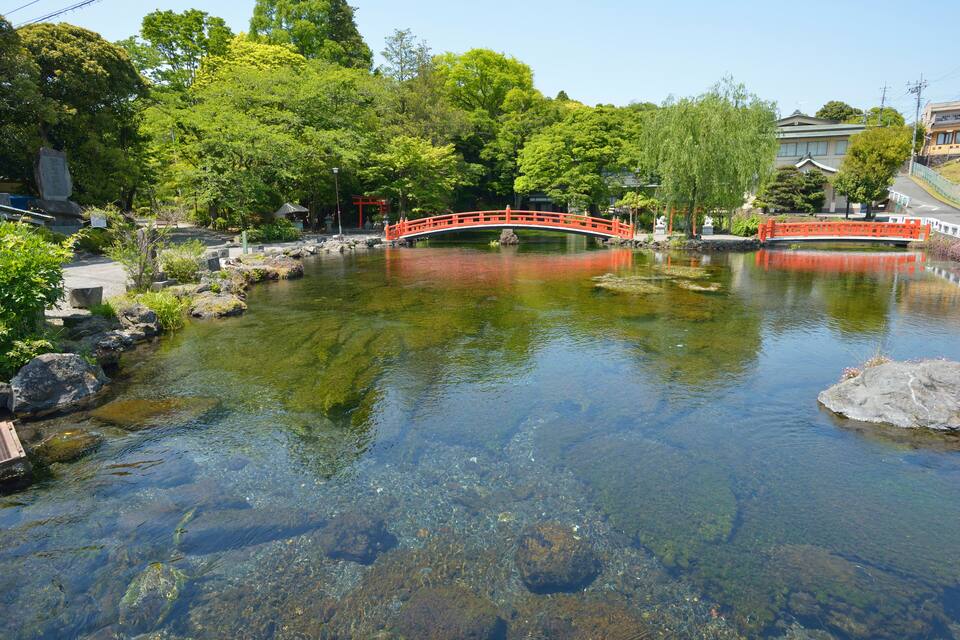 A clear river with a red bridge, surrounded by lush greenery and traditional buildings.