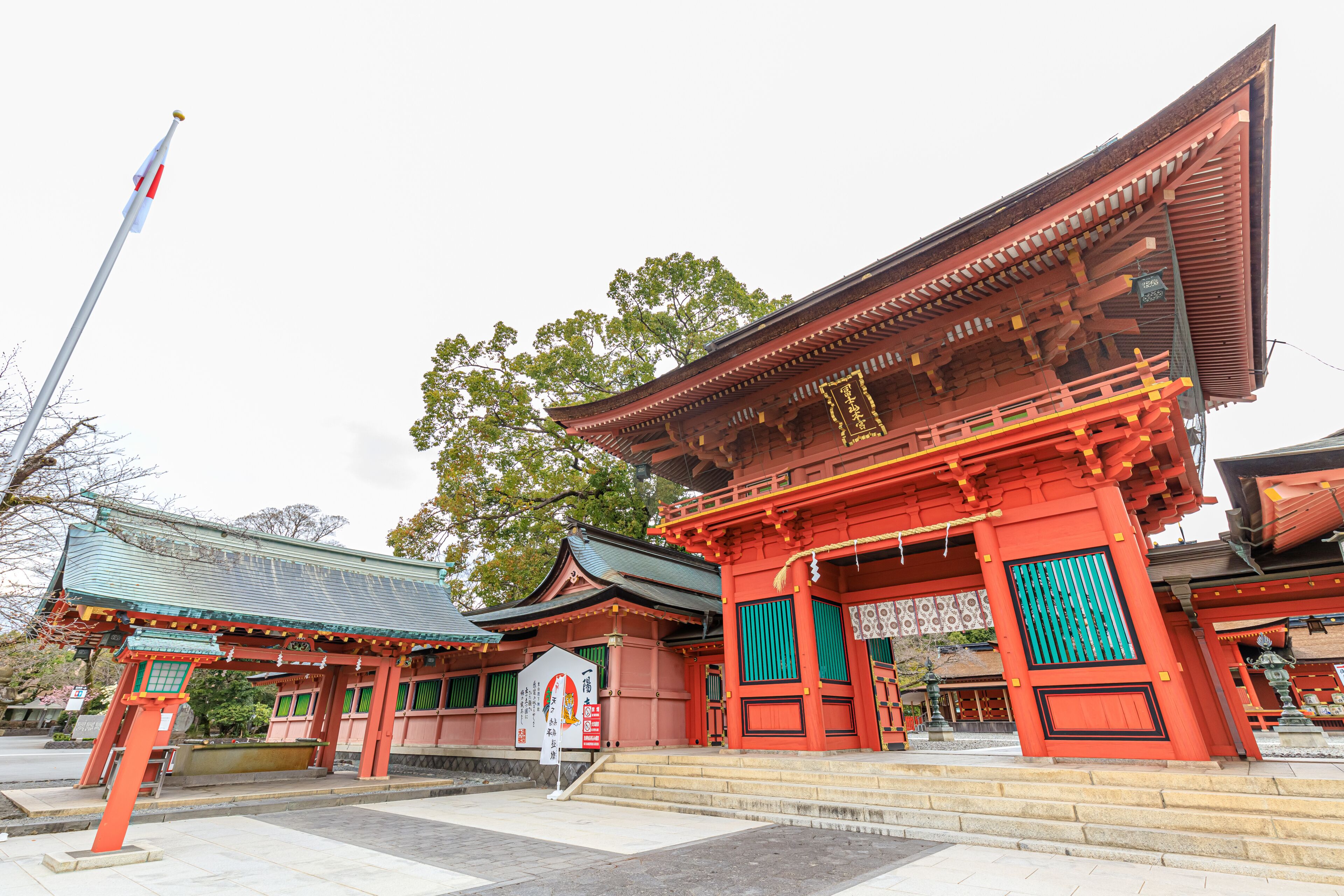 A traditional Japanese temple with red and green accents, a stone lantern, and a flagpole.