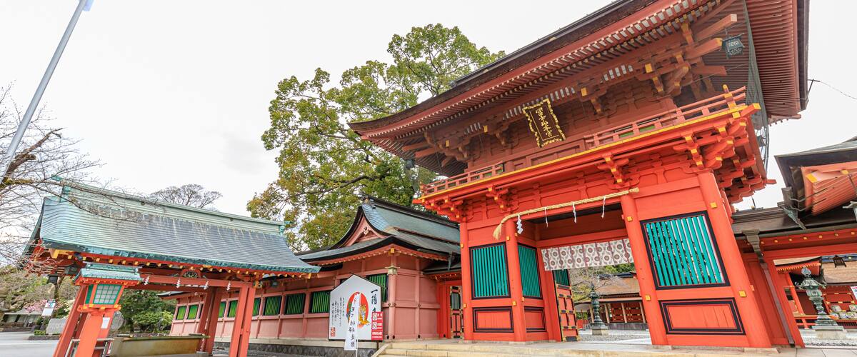 A traditional Japanese temple with red and green accents, a stone lantern, and a flagpole.