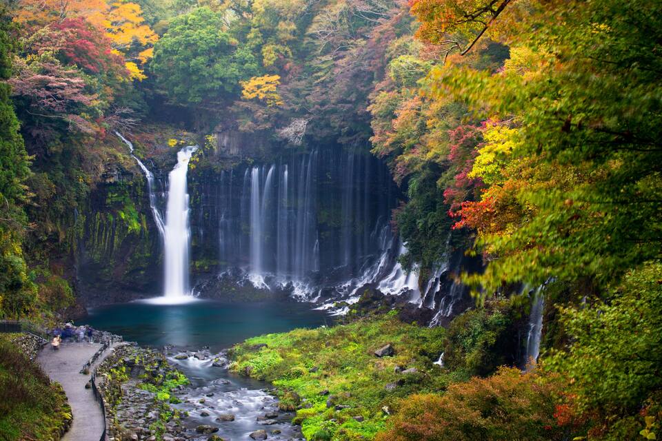 Een meerlaagse waterval omringd door weelderige herfstkleuren.
