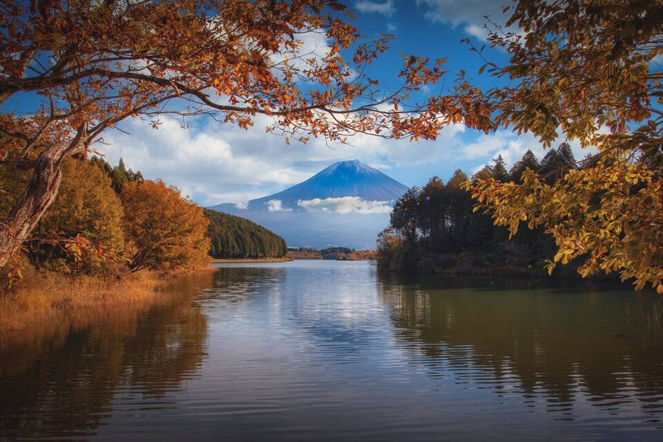 A calm lake with autumn foliage and a mountain in the background.