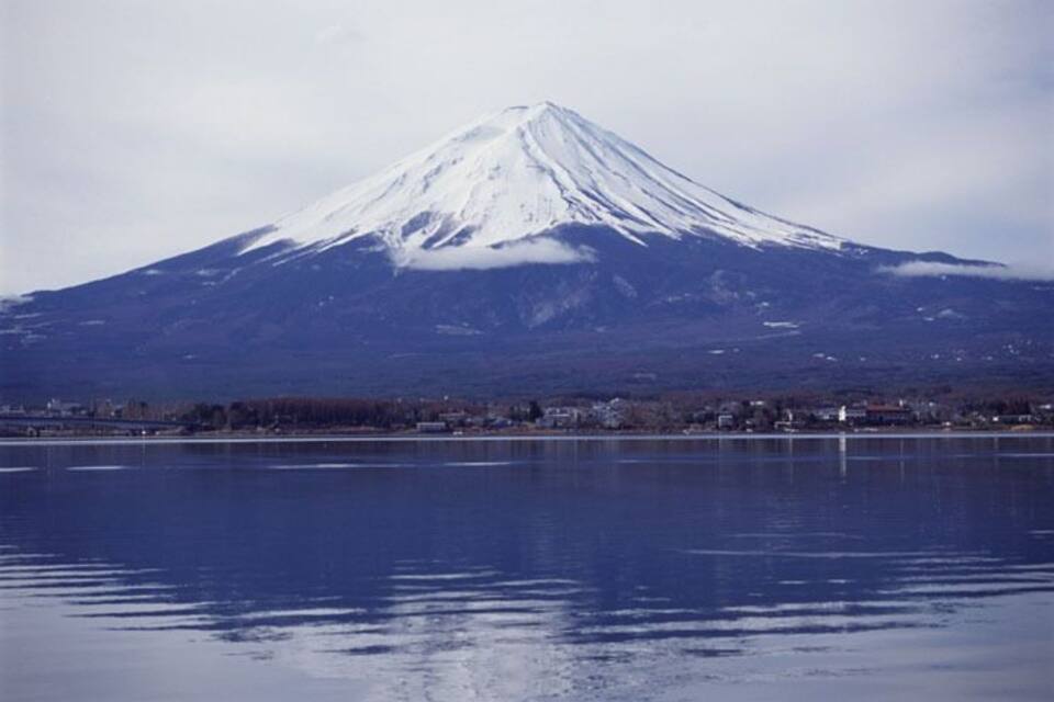 A snow-capped mountain with a lake in the foreground.
