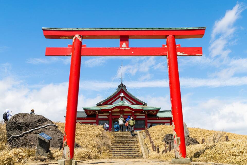 Um portão torii vermelho que dá acesso a um edifício tradicional japonês com telhado de telhas.