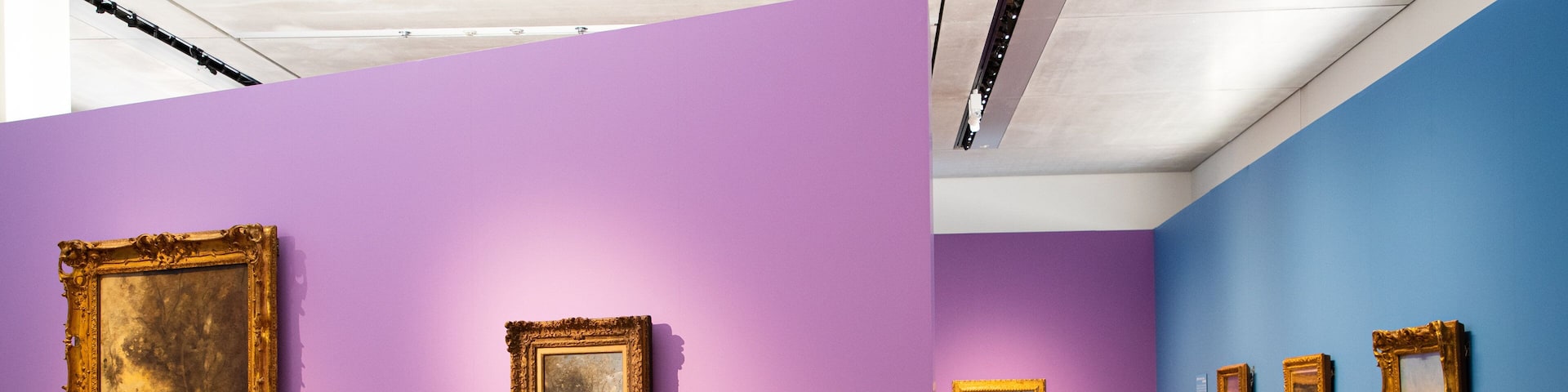 Una galería de arte con paredes moradas y azules, mostrando varias pinturas enmarcadas.