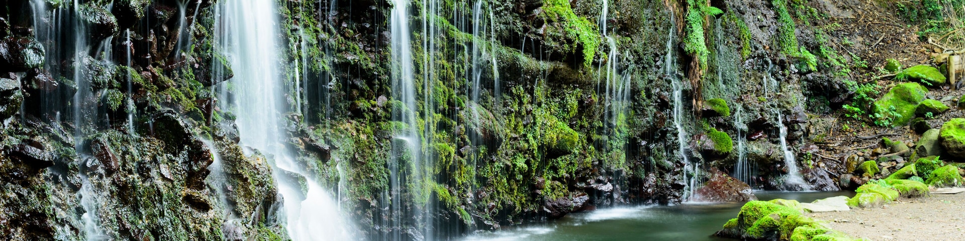 Une cascade à plusieurs niveaux dévalant des rochers couverts de mousse et se jetant dans une rivière paisible.
