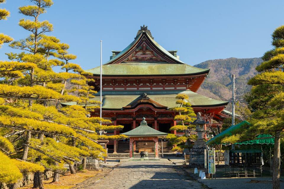 A traditional Japanese temple with a multi-tiered roof, surrounded by pine trees.