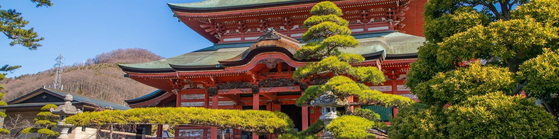 A traditional Japanese temple with a curved roof, surrounded by lush greenery and stone lanterns.