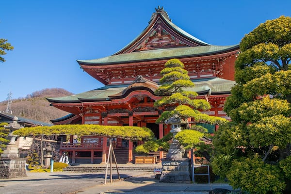 Un temple japonais traditionnel, doté d’un toit incurvé, entouré d’une végétation luxuriante et de lanternes en pierre.