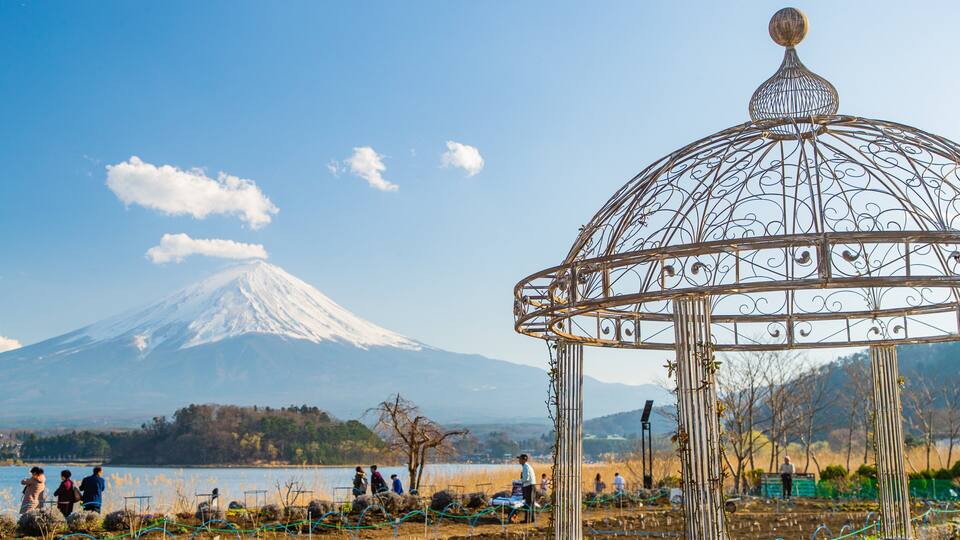 A metal gazebo with a decorative top, a snow-capped mountain in the background, and a lake with people in the foreground.