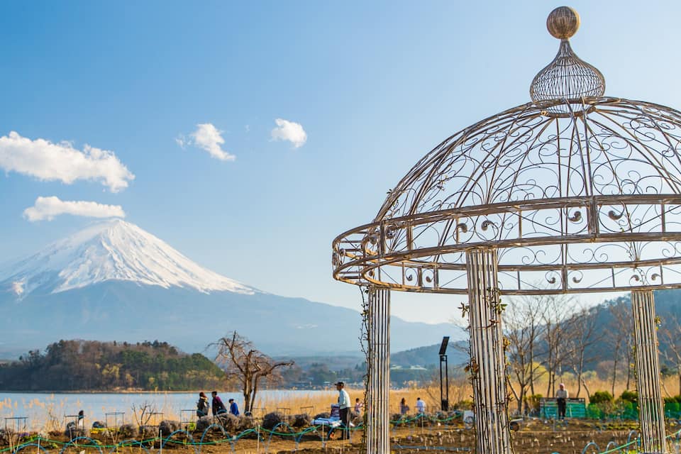 A metal gazebo with a decorative top, a snow-capped mountain in the background, and a lake with people in the foreground.