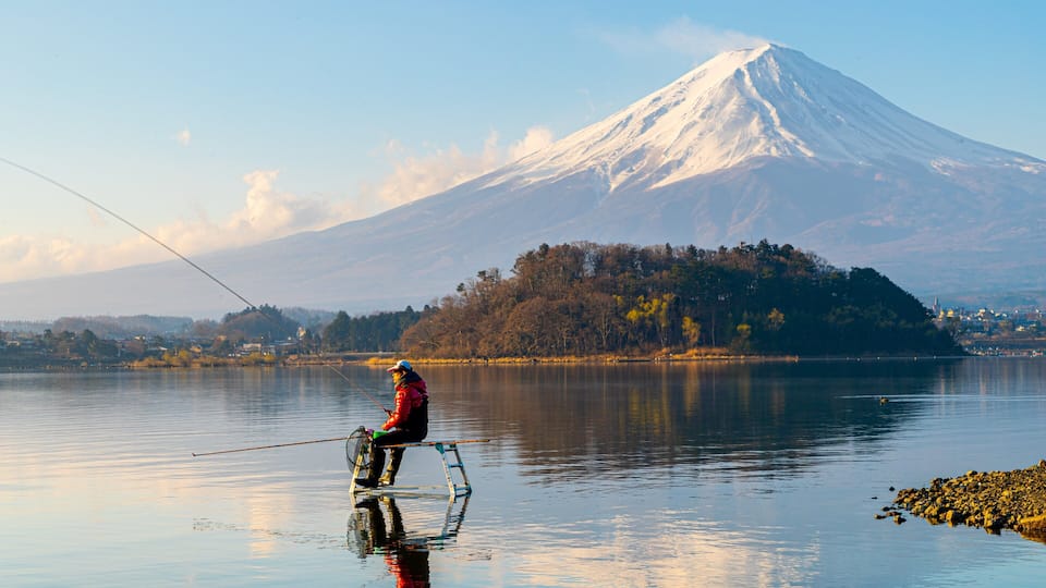 A person fishing on a boat with a snow-capped mountain in the background.