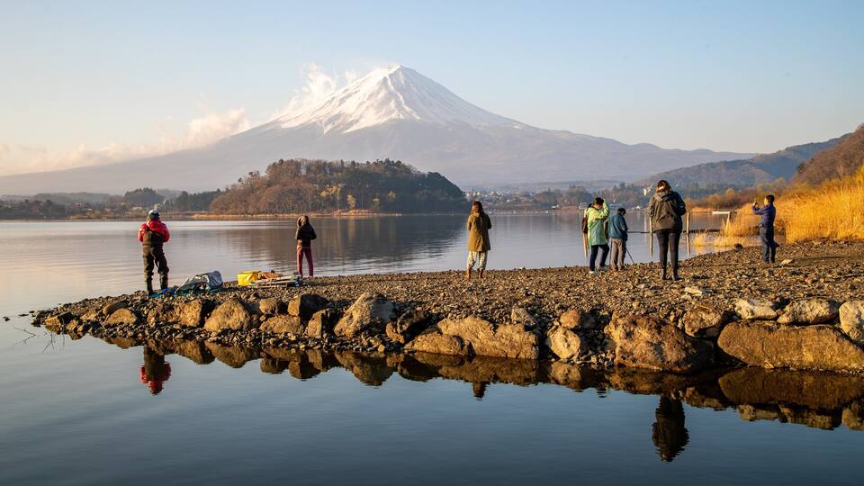 A group of people on a rocky lakeshore with a snow-capped mountain in the background.