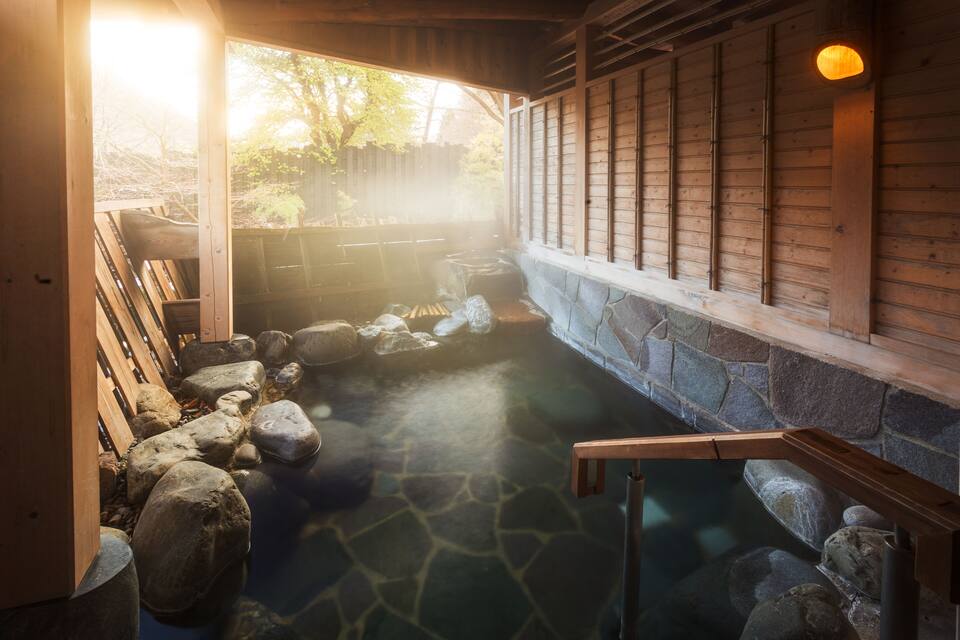 Uma onsen japonesa tradicional com uma passarela de madeira, degraus de pedra e uma parede de pedra.