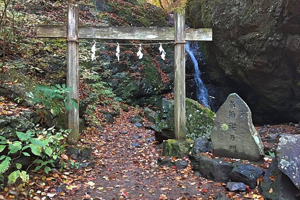 Een houten boogdoorgang met hangende papieren decoraties, een stenen gedenksteen met inscripties en een waterval.