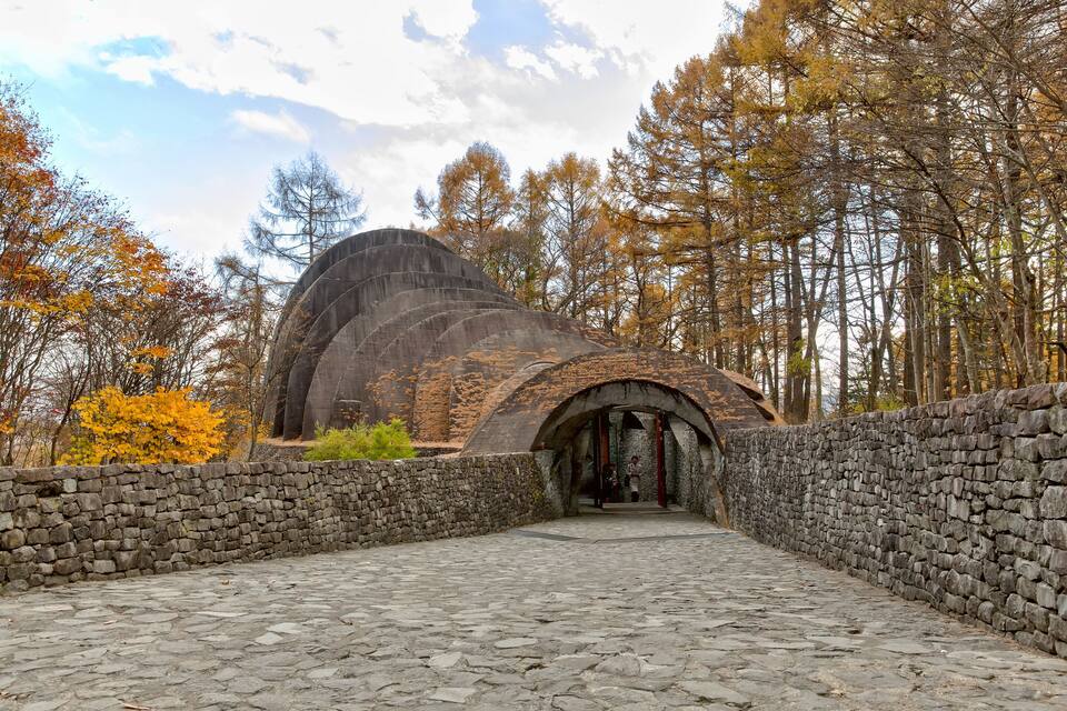 A stone pathway leading to a domed structure surrounded by autumn trees.