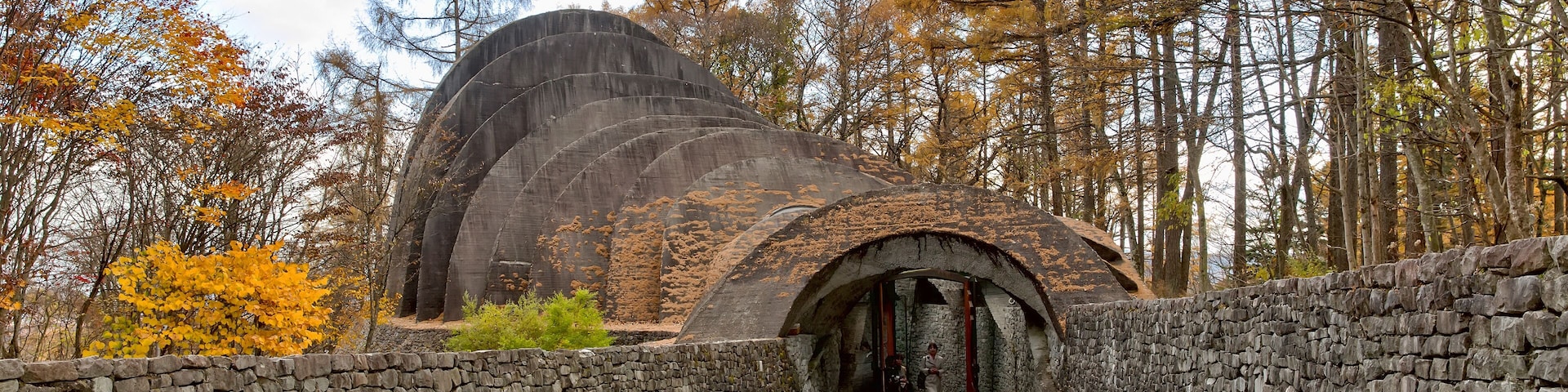 Uma trilha de pedra leva a uma estrutura em forma de cúpula, rodeada por árvores de outono.