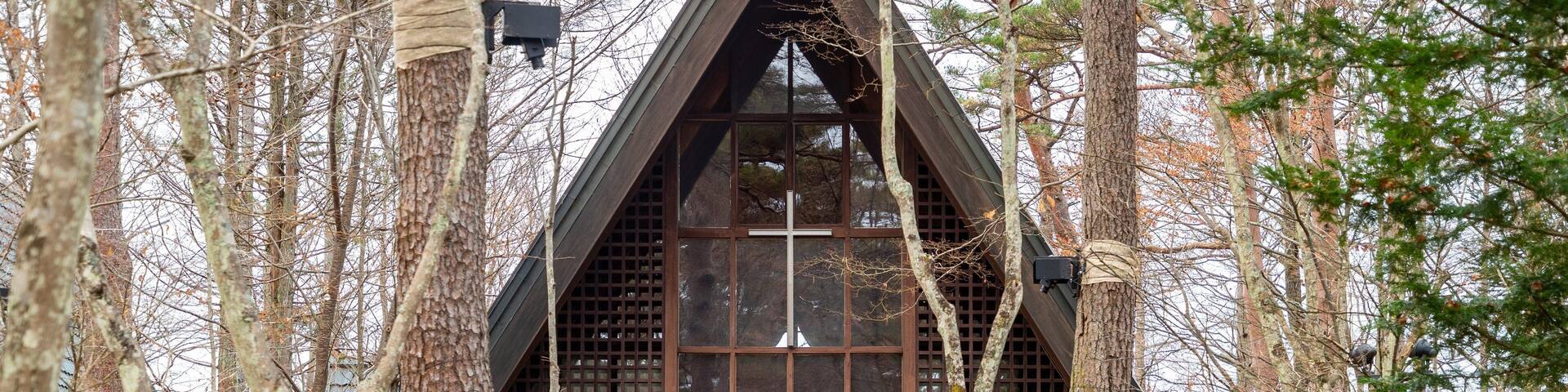 A wooden chapel with a cross, surrounded by trees.