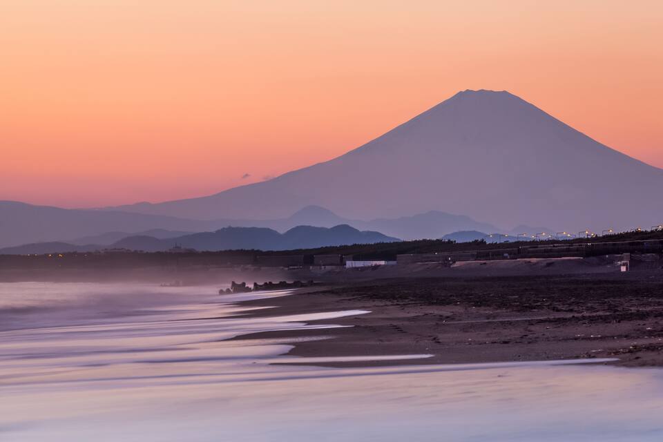 Una montaña al atardecer con una playa en primer plano.