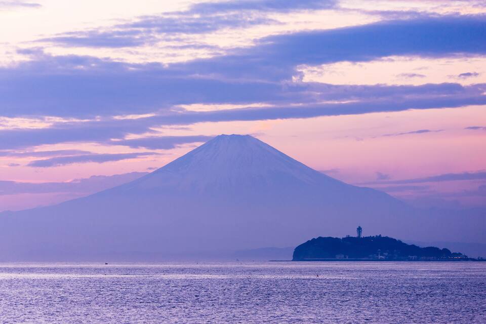 A mountain with a lighthouse on a small island in the foreground.