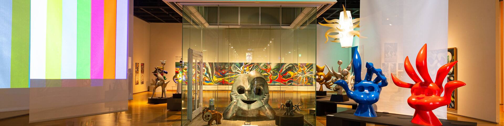Una galería de arte con coloridas esculturas abstractas y una gran pantalla digital.