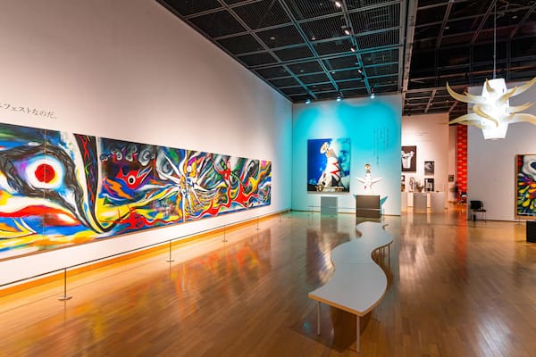 An art gallery with large colorful paintings on the walls and a wooden floor.