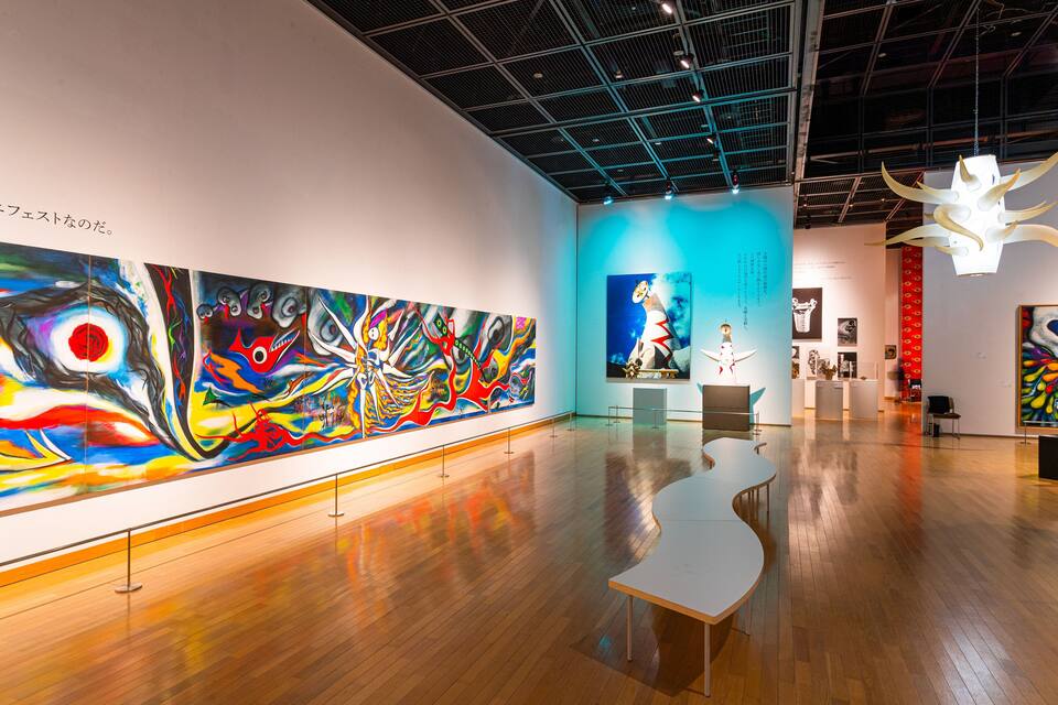 Eine Kunstgalerie mit großen, farbenfrohen Gemälden an den Wänden und einem Holzboden.
