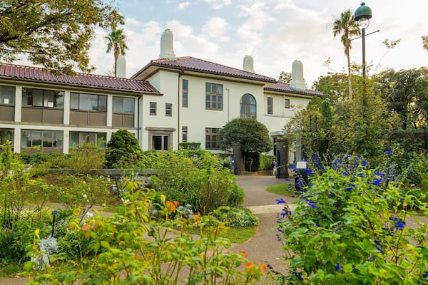 A large, two-story building with a red-tiled roof, surrounded by lush gardens and trees.