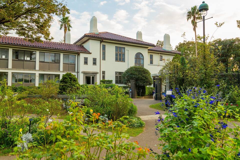 A large, two-story building with a red-tiled roof, surrounded by lush gardens and trees.