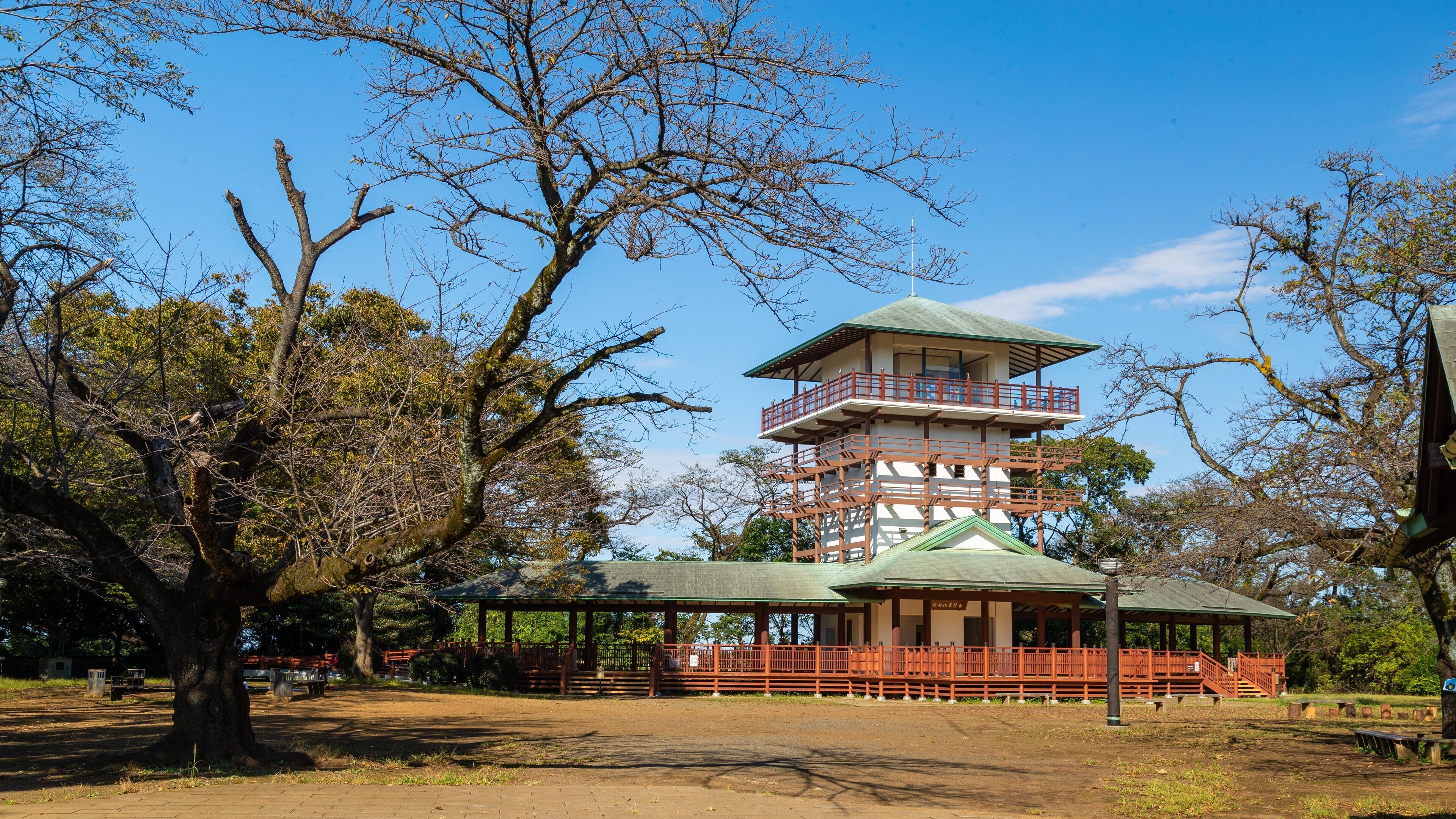 Una pagoda japonesa tradicional con techo verde, rodeada de árboles y una valla de madera.