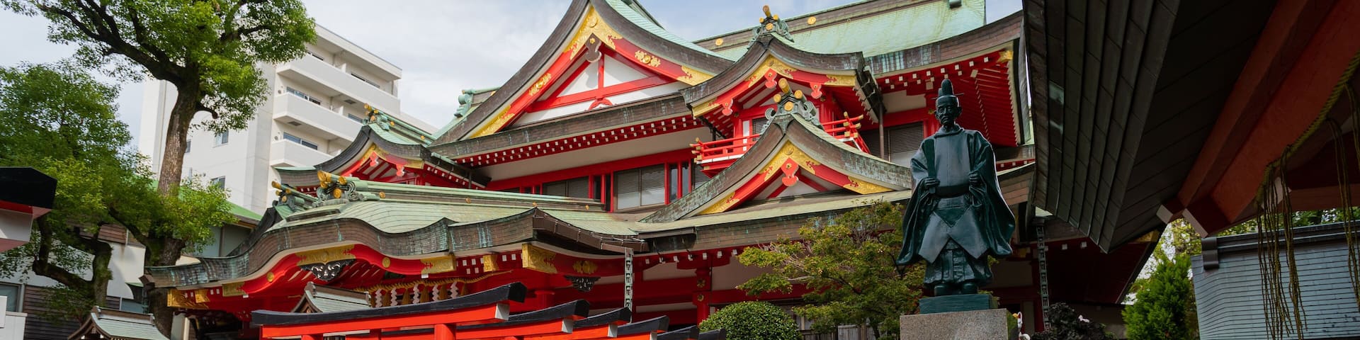 A traditional Japanese temple with red torii gates, a stone statue, and a multi-tiered roof.