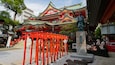 A traditional Japanese temple with red torii gates, a stone statue, and a multi-tiered roof.