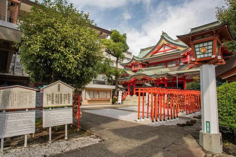 A traditional Japanese temple with red torii gates, a stone lantern, and informational signs.