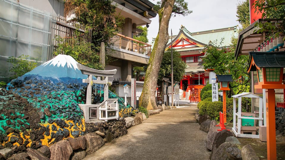 Un santuario japonés tradicional con una pintura de montaña colorida, una puerta torii de piedra y un camino que lleva a la entrada.