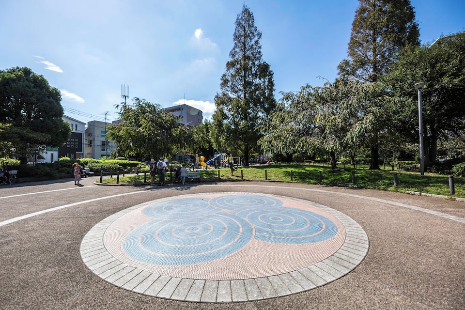 A park with a circular mosaic design, trees, and a playground.