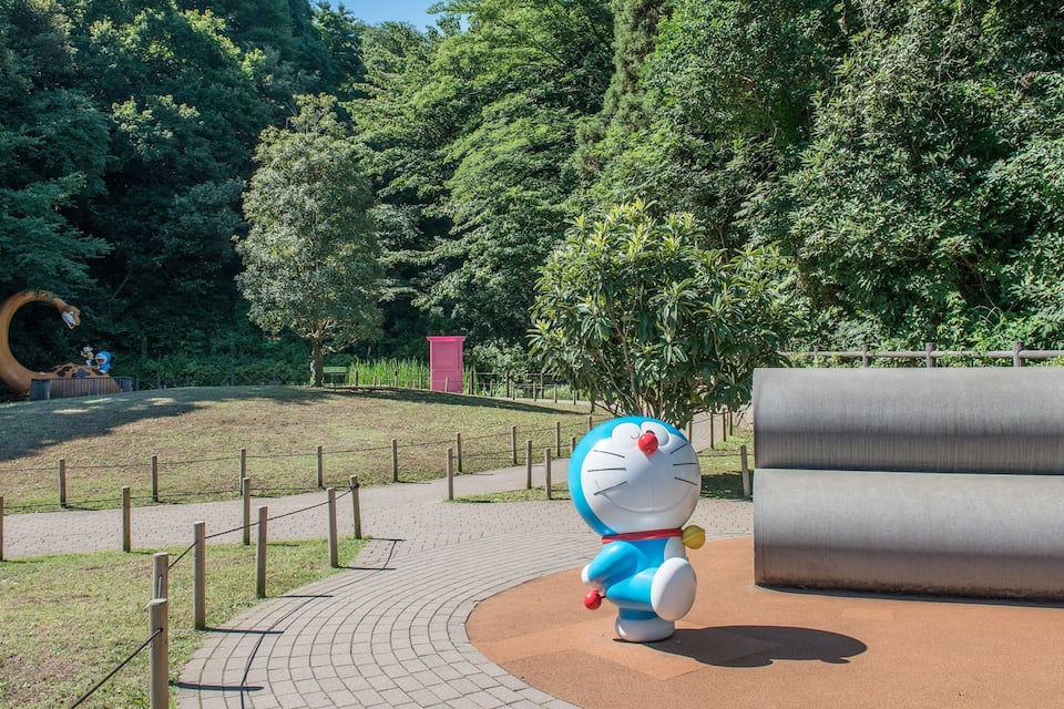 A park with a large sculpture of a cartoon character, a winding path, and a large grey bench.