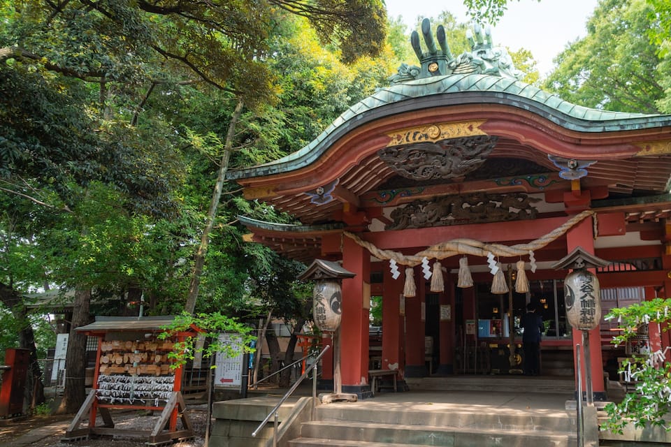A traditional Japanese temple with a curved roof, red pillars, and a wooden staircase leading up to the entrance.