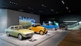 Vintage cars on display in a modern museum with a large digital screen in the background.