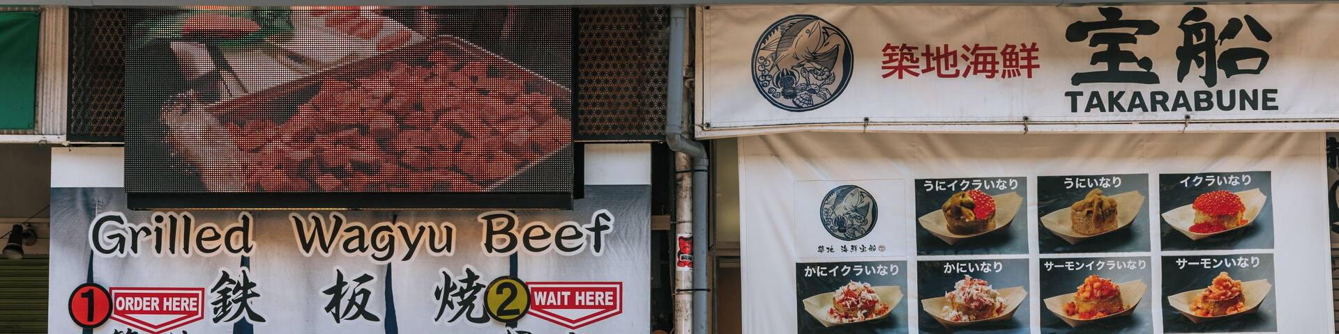 A busy street with a food stall advertising grilled wagyu beef and another with takarabune.