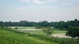 A golf course with a well-maintained green, sand bunkers, and a clear sky.
