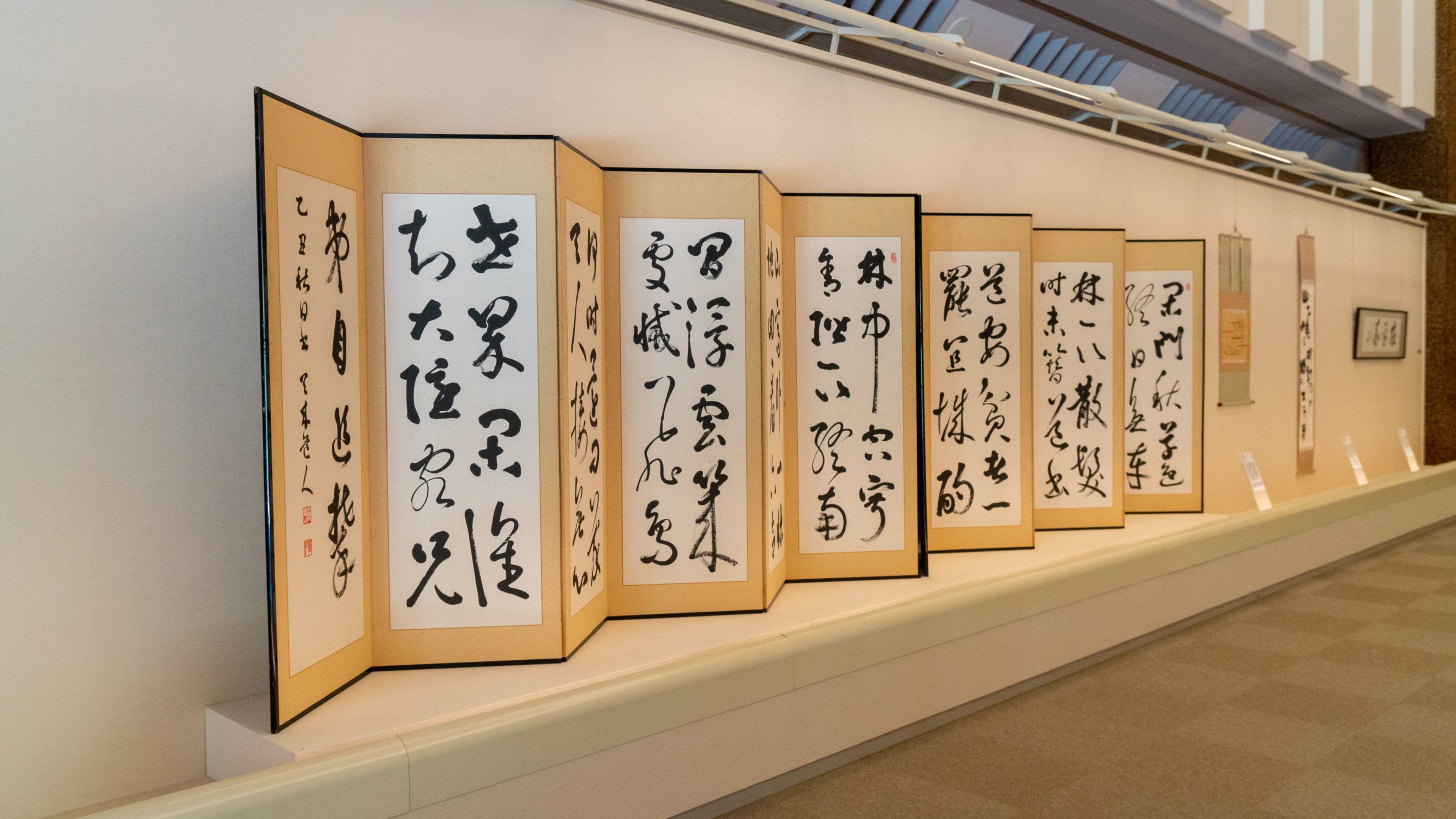 A series of traditional Japanese calligraphy scrolls displayed on a wall in a gallery.