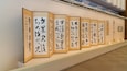 Eine Reihe traditioneller japanischer Schriftrollen, die an einer Galeriewand ausgestellt sind.