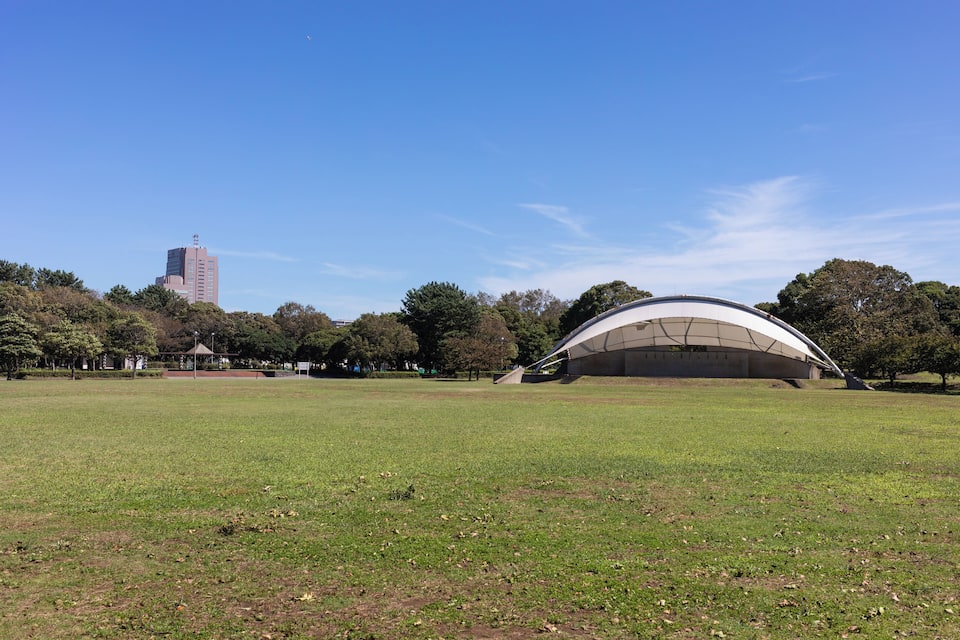 Un parque con un amplio espacio abierto, una estructura arquitectónica moderna y un edificio alto al fondo.