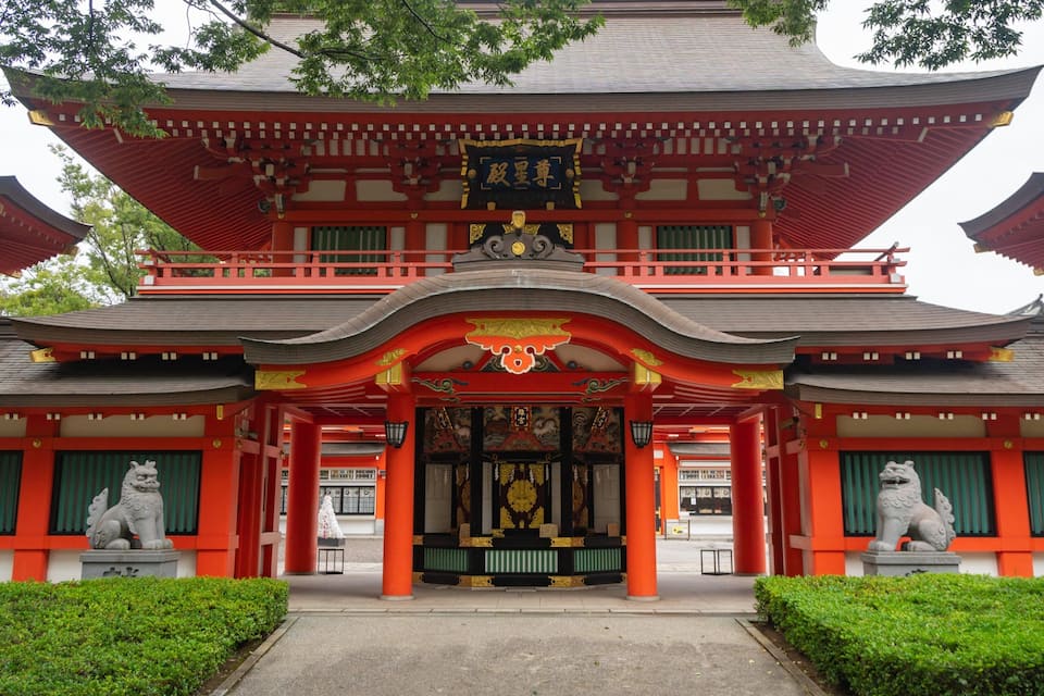Un templo japonés tradicional con detalles en rojo y dorado, un santuario central y dos estatuas de leones en la entrada.