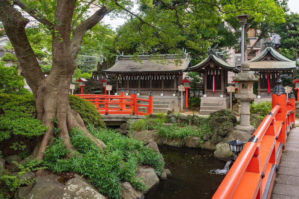 A traditional Japanese temple with a red torii gate, a stone lantern, and a small pond.