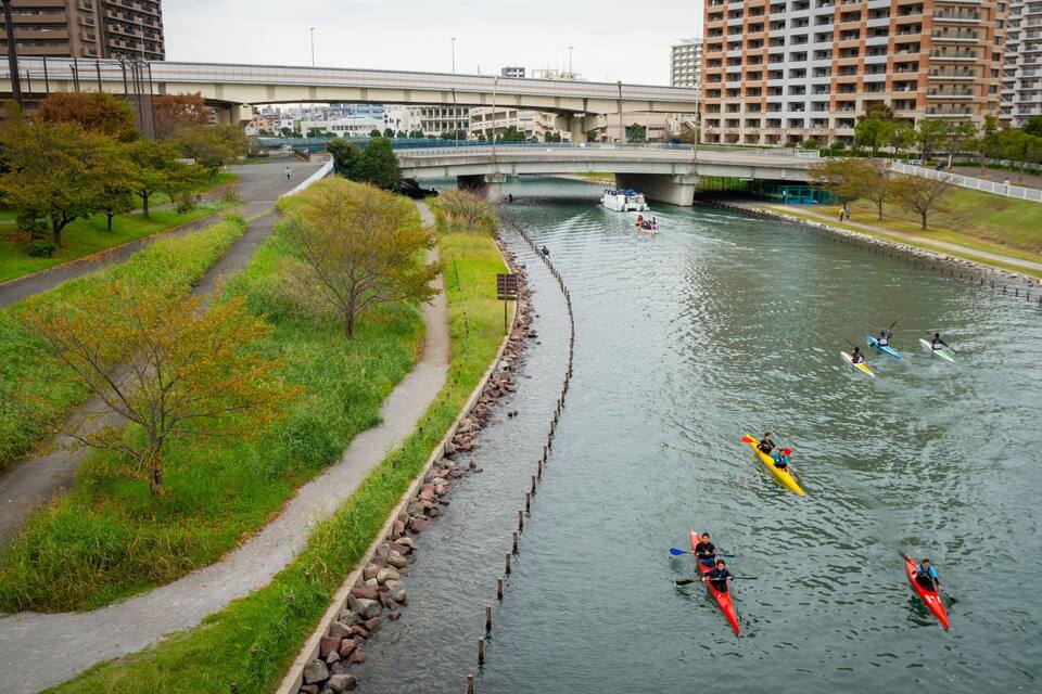 Un río con kayakistas, un puente y edificios urbanos al fondo.