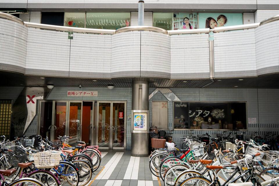 A covered bicycle parking area with a tiled roof and a storefront with a sign in a foreign language.