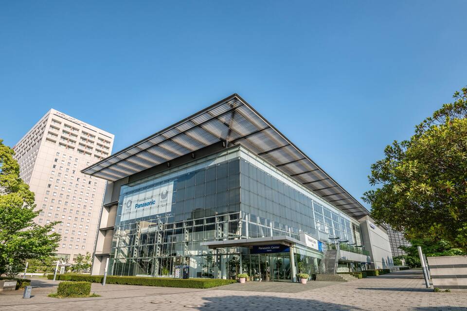 Een modern glazen gebouw met een blauw bord waarop 'Panasonic Center' staat.