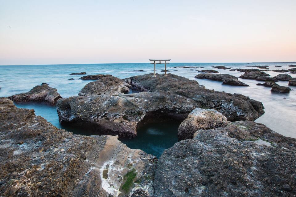 A rocky shoreline with a traditional Japanese torii gate.